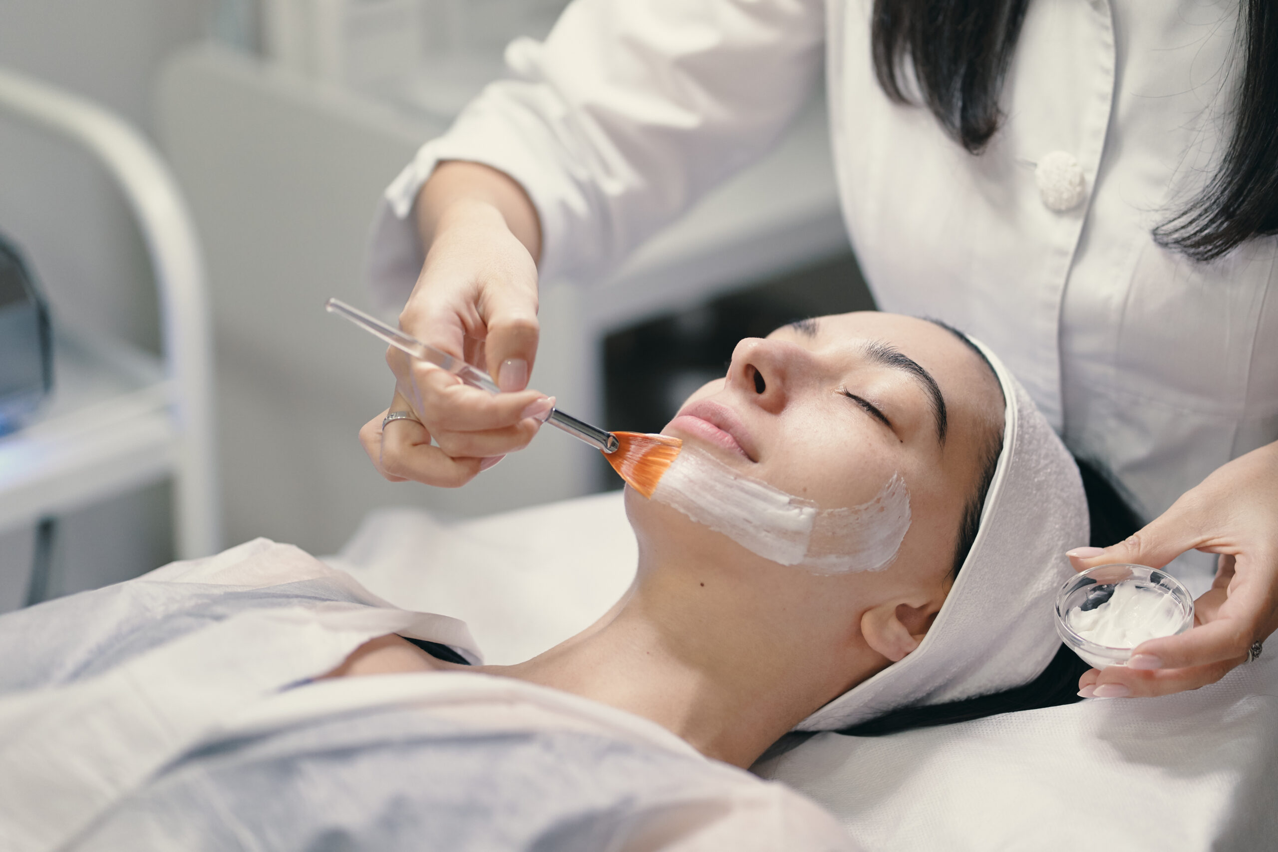 People, beauty, spa, cosmetology and skin care concept - Cosmetologist applying cream on a woman beautiful face with a cosmetologist brush.